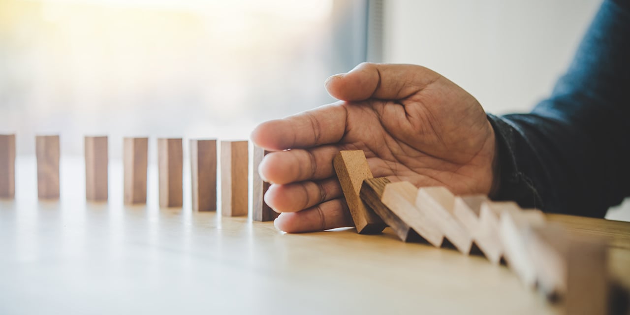 Photograph of an adult hand knocking over a string of dominoes.