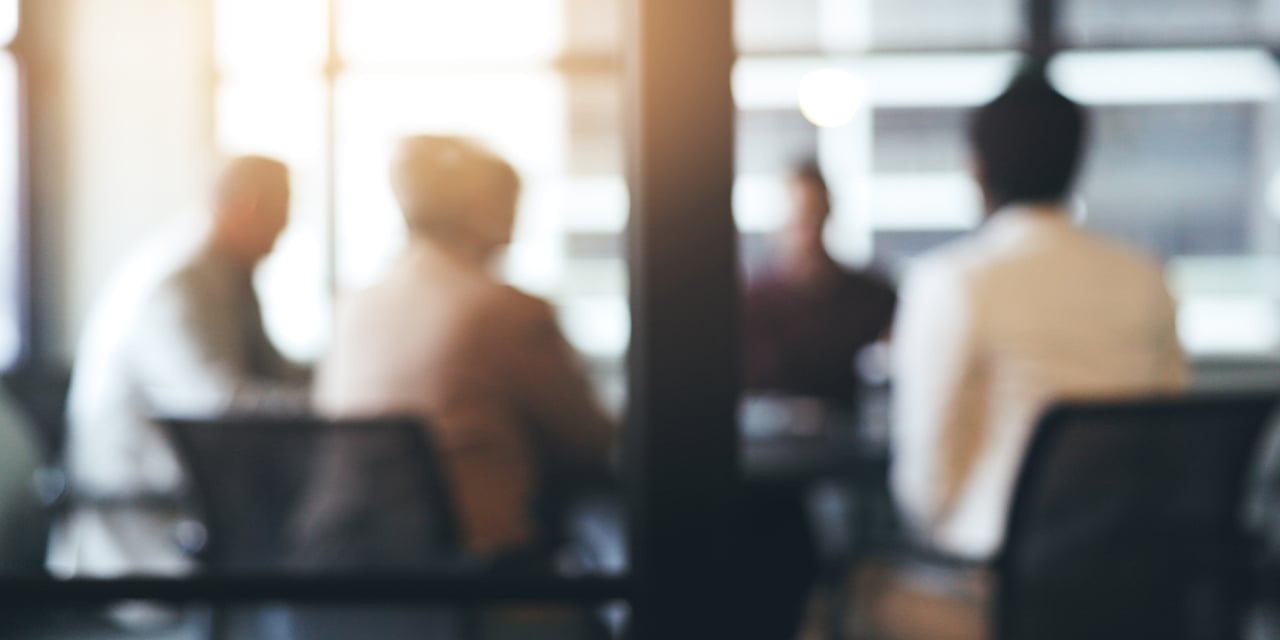 Blurred image of people sitting at a conference room table.